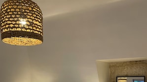 A bedroom with a large bed, two bedside lamps, a hanging light fixture, a mirror, and a view of the outside.