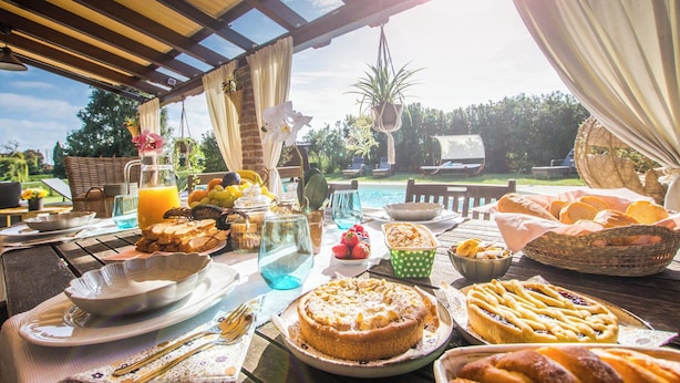 An outdoor breakfast setting with a table set for breakfast, including bread, pastries, and fruit.