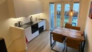 A modern kitchen with a central island, a dining area with a table and chairs, and a view through large windows. - Stylish House in Breda city center (Breda)