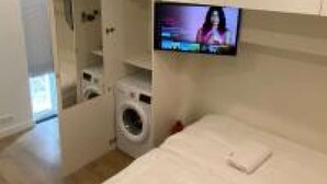A modern bedroom with a built-in washing machine, a TV mounted on the wall, and a large bed. - Stylish House in Breda city center (Breda)