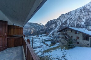 A wooden balcony overlooking a snow-covered village with stone buildings and mountains in the background. - Welcoming 3BR Flat with parking in Verrand (Pre-Saint-Didier)