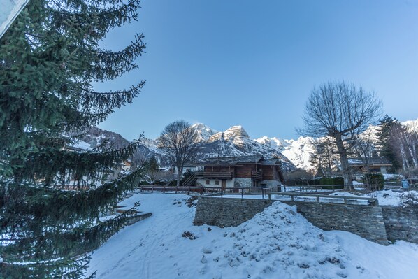 A snow-covered landscape with a wooden building, a stone wall, and snow-covered mountains in the background. - Welcoming 3BR Flat with parking in Verrand (Pre-Saint-Didier)