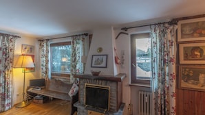 Ein gemütliches Wohnzimmer mit Kamin, floralem Vorhang und Blick ins Freie.
