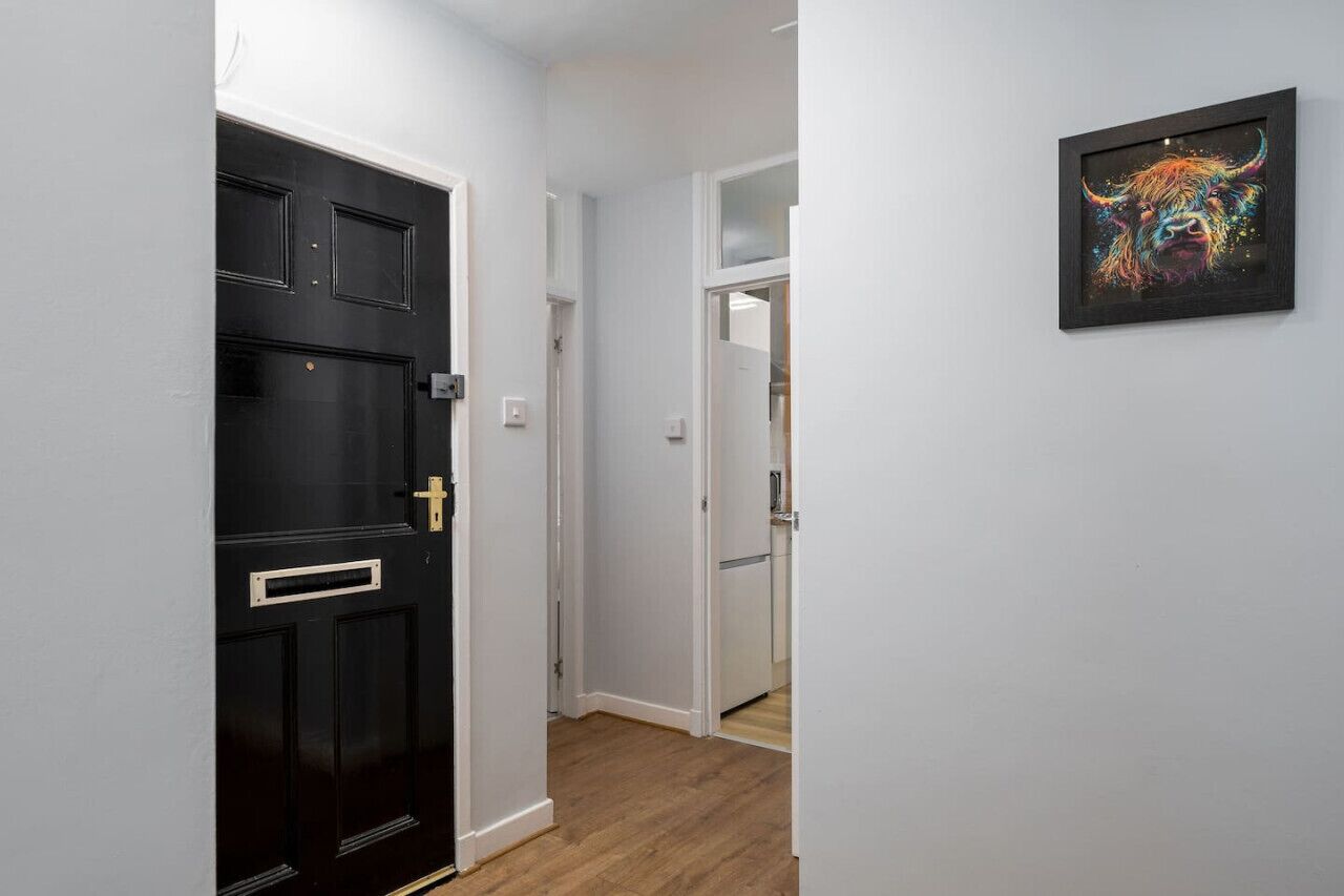 A hallway with a black door, a white wall, and a framed artwork.