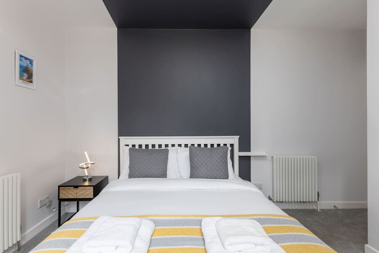 Una habitación de hotel moderna con una cama blanca, cabecera gris y colcha a rayas.