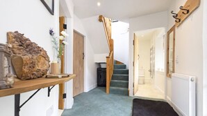 Un couloir avec un escalier en bois, un radiateur et un tapis noir menant à une salle de bain.