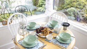 Une table à manger dressée avec de la vaisselle verte : assiettes, bols et couverts, et une vue sur la verdure à l’extérieur.