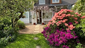 Une maison avec un chemin de jardin menant à une porte, entourée d’une végétation luxuriante et de plantes en fleurs.