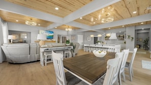 A spacious living area with a wooden ceiling, a dining table surrounded by chairs, a sofa, and a kitchen area with white cabinets and a large island. - Hidden Valley Paradise (Glaze Township)