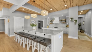 A modern kitchen with a central island, bar stools, pendant lights, and a clock on the wall. - Hidden Valley Paradise (Glaze Township)