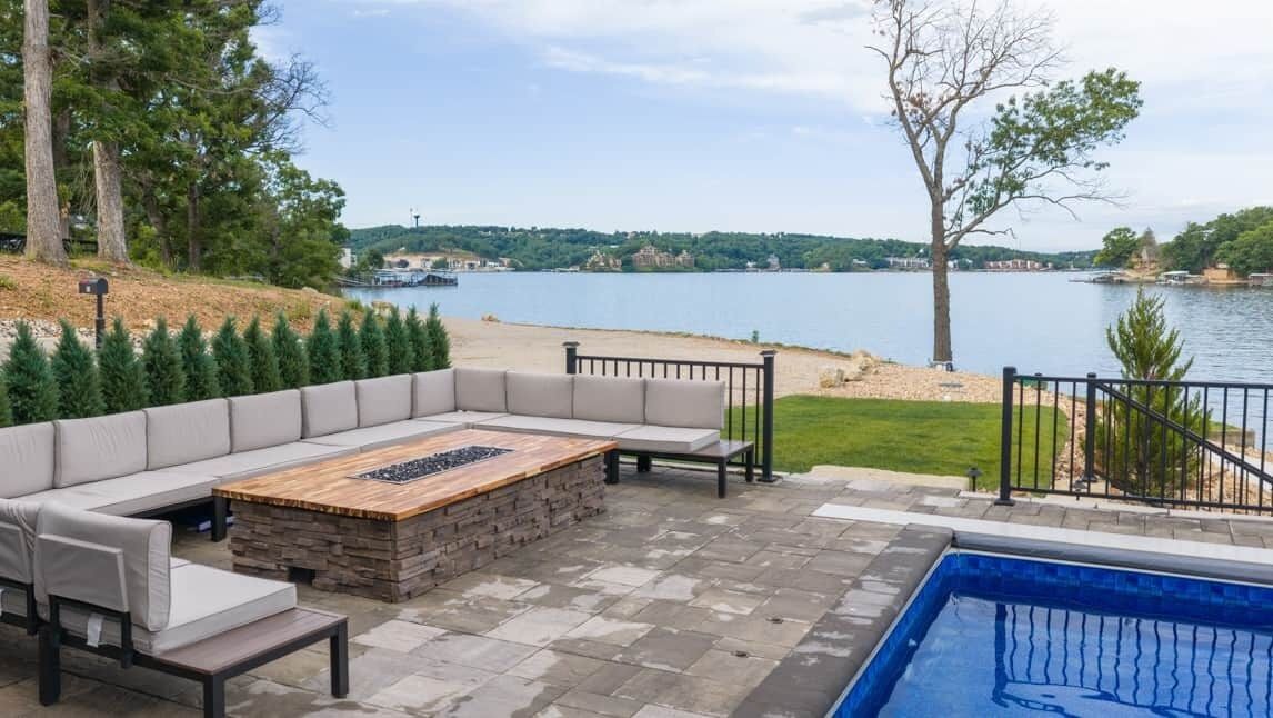 An outdoor seating area with a pool, a wooden table, and a view of a lake.
