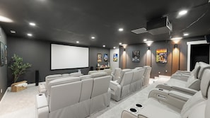 Un cine en casa con una pantalla grande, sillones reclinables y carteles de películas en la pared.