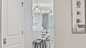 A hallway with a white door, a kitchen area with a marble countertop, and a dining area with bar stools.