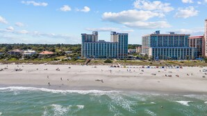 A beachfront hotel with multiple high-rise buildings, a sandy beach, and ocean waves.