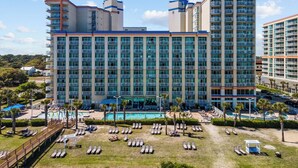 A multi-story hotel with a pool area, sun loungers, and a view of the surrounding landscape.