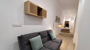 En moderne stue med en grå sofa, et træskab og en gulvlampe.
