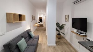 En moderne stue med en grå sofa, et ophængt fjernsyn og en træhylde.