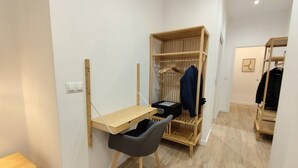 Et lille værelse med skrivebord i træ, stol, garderobe og knagerække.