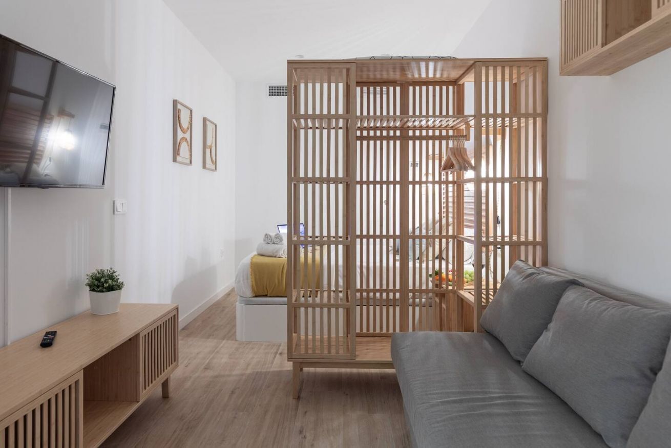 A modern living room with a grey sofa, wooden floor, a TV mounted on the wall, and a wooden partition with a ladder.