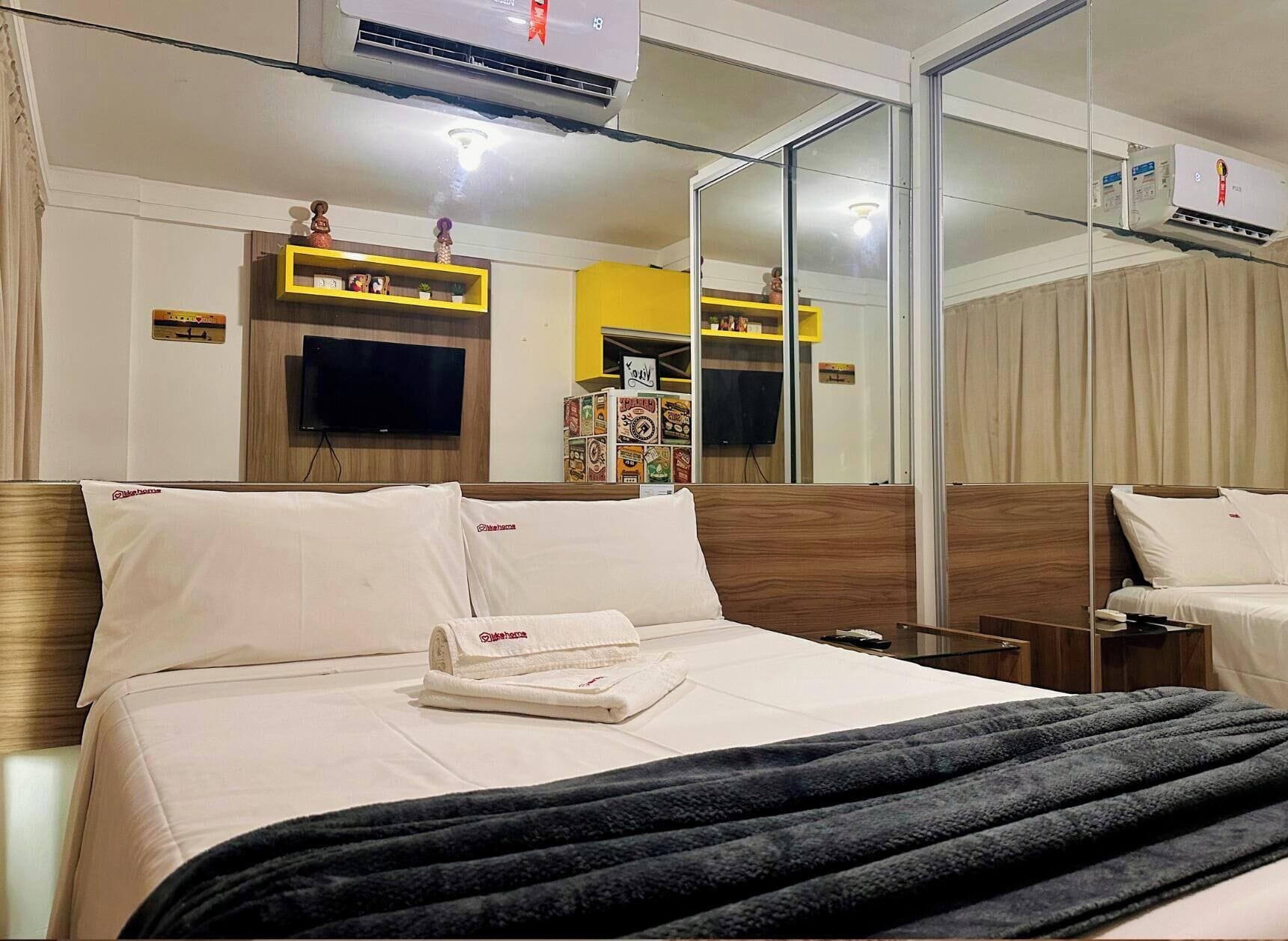 A hotel room with a bed, a TV, a mirror, and a minibar.