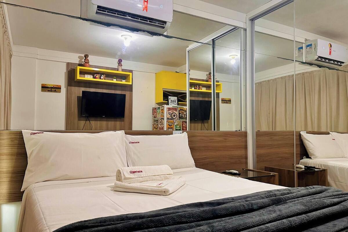 A hotel room with a bed, a TV, a mirror, and a minibar.