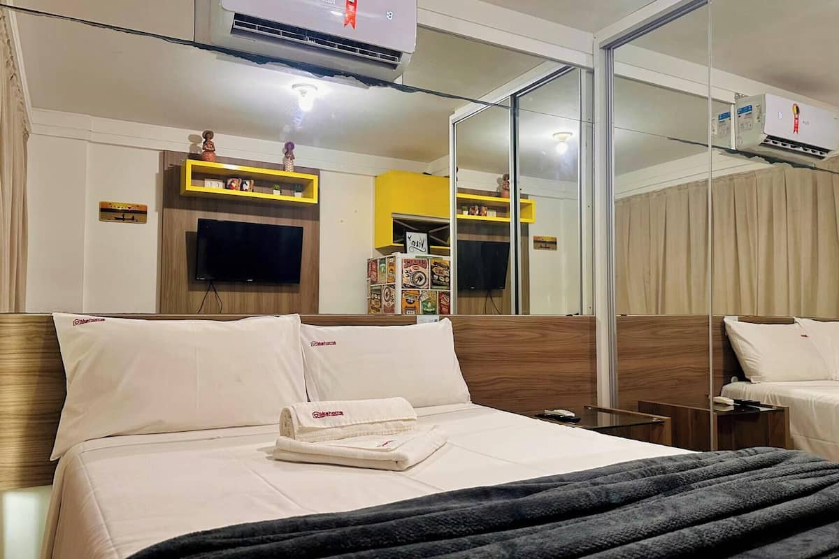 A hotel room with a bed, a TV, a mirror, and a minibar.