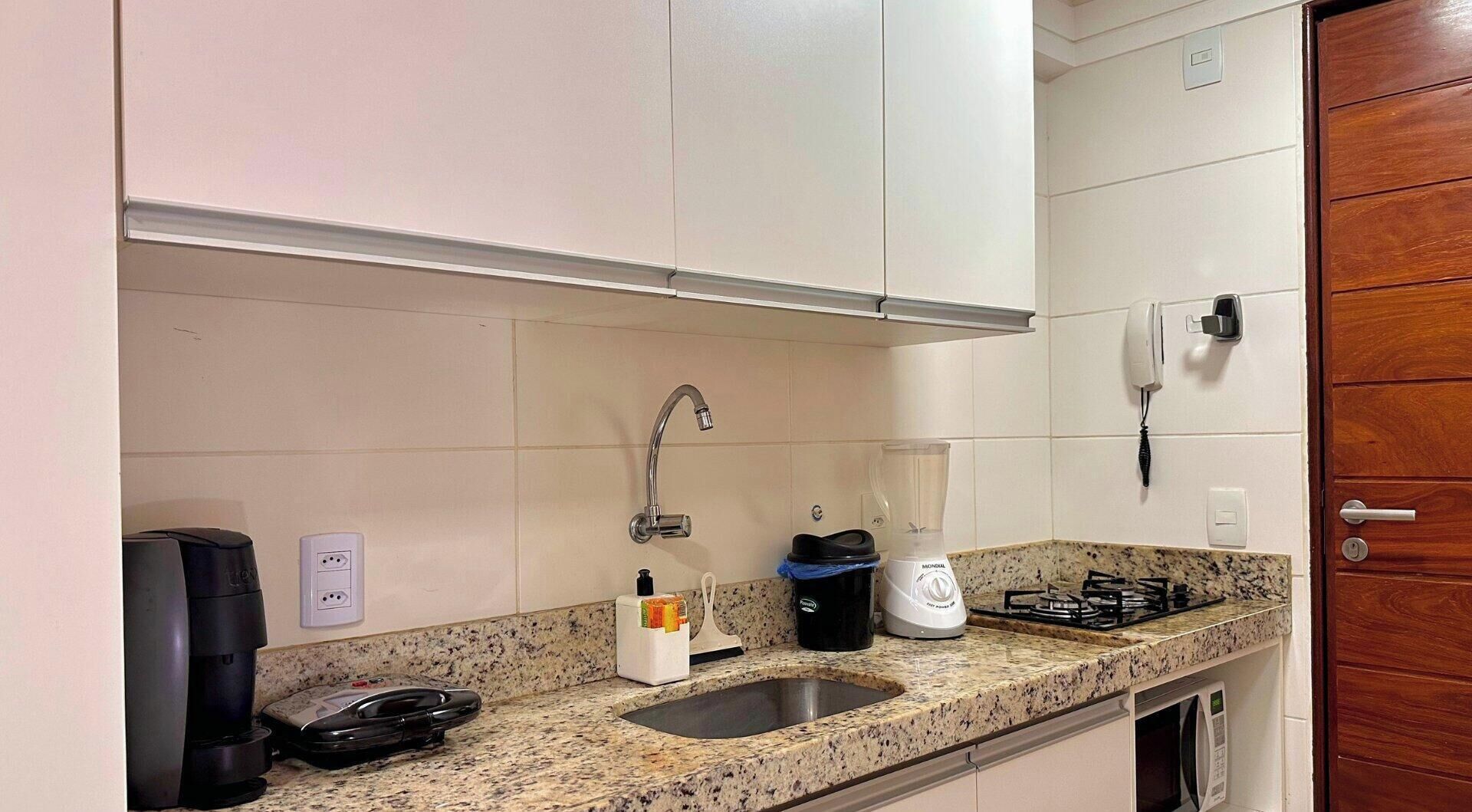 Una cocina con encimera de granito, pileta de acero inoxidable, cafetera, licuadora y estufa.
