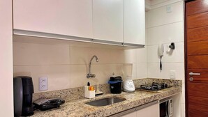 Una cocina con encimera de granito, pileta de acero inoxidable, cafetera, licuadora y estufa.