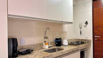 Una cocina con encimera de granito, pileta de acero inoxidable, cafetera, licuadora y estufa.
