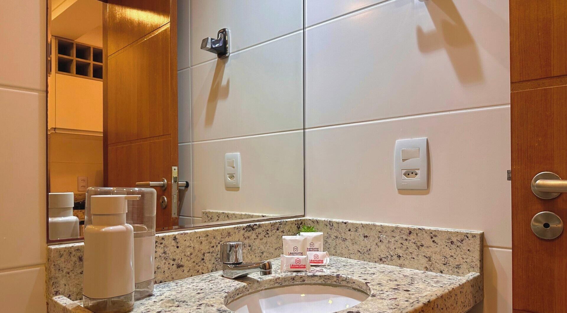 Un baño con encimera de granito, lavabo, espejo y puerta de madera.