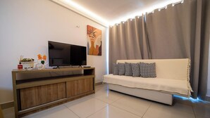 Una sala de estar moderna con una televisión de pantalla plana sobre un soporte de madera, un sofá con cojines estampados y un ventanal con cortinas.