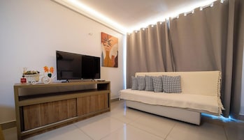 Una sala de estar moderna con una televisión de pantalla plana sobre un soporte de madera, un sofá con cojines estampados y un ventanal con cortinas.