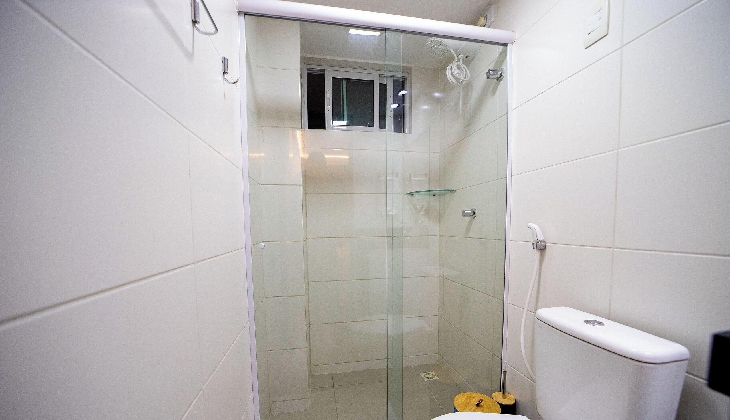Un baño con cabina de ducha de vidrio, un inodoro y un taburete de madera.