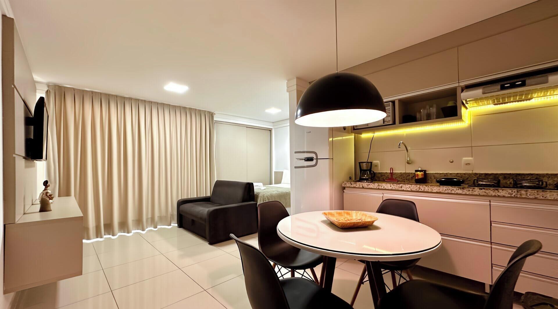 Una habitación de hotel moderna con zona de comedor, sofá, televisor y cocina equipada con microondas.