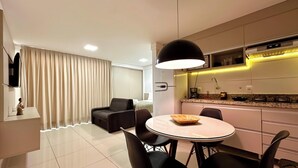 Una habitación de hotel moderna con zona de comedor, sofá, televisor y cocina equipada con microondas.