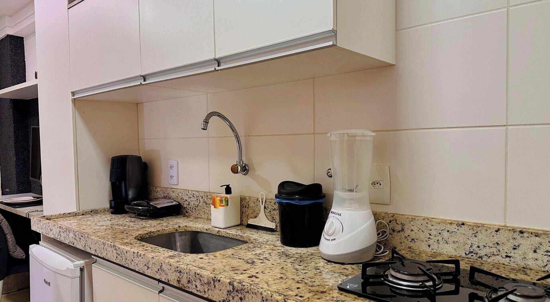 Una cocina con encimera de granito, un fregadero, cafetera, licuadora y estufa.