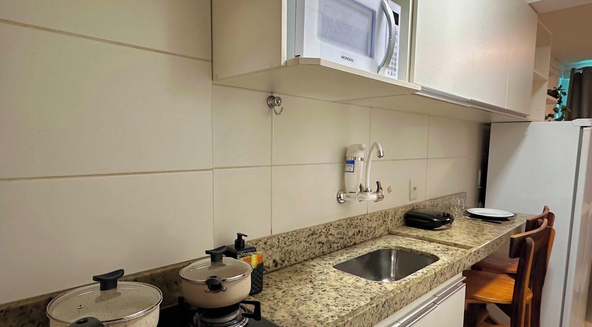 Una cocina con armarios blancos, encimera de granito, pileta, estufa y microondas.