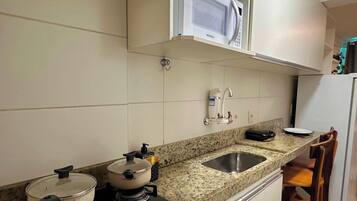 Una cocina con armarios blancos, encimera de granito, pileta, estufa y microondas.