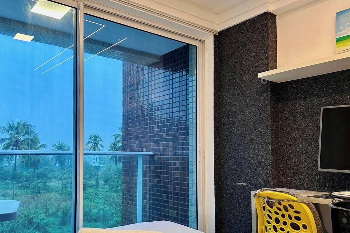 A room with a sliding glass door leading to a balcony, a small table with a chair, and a TV mounted on the wall.