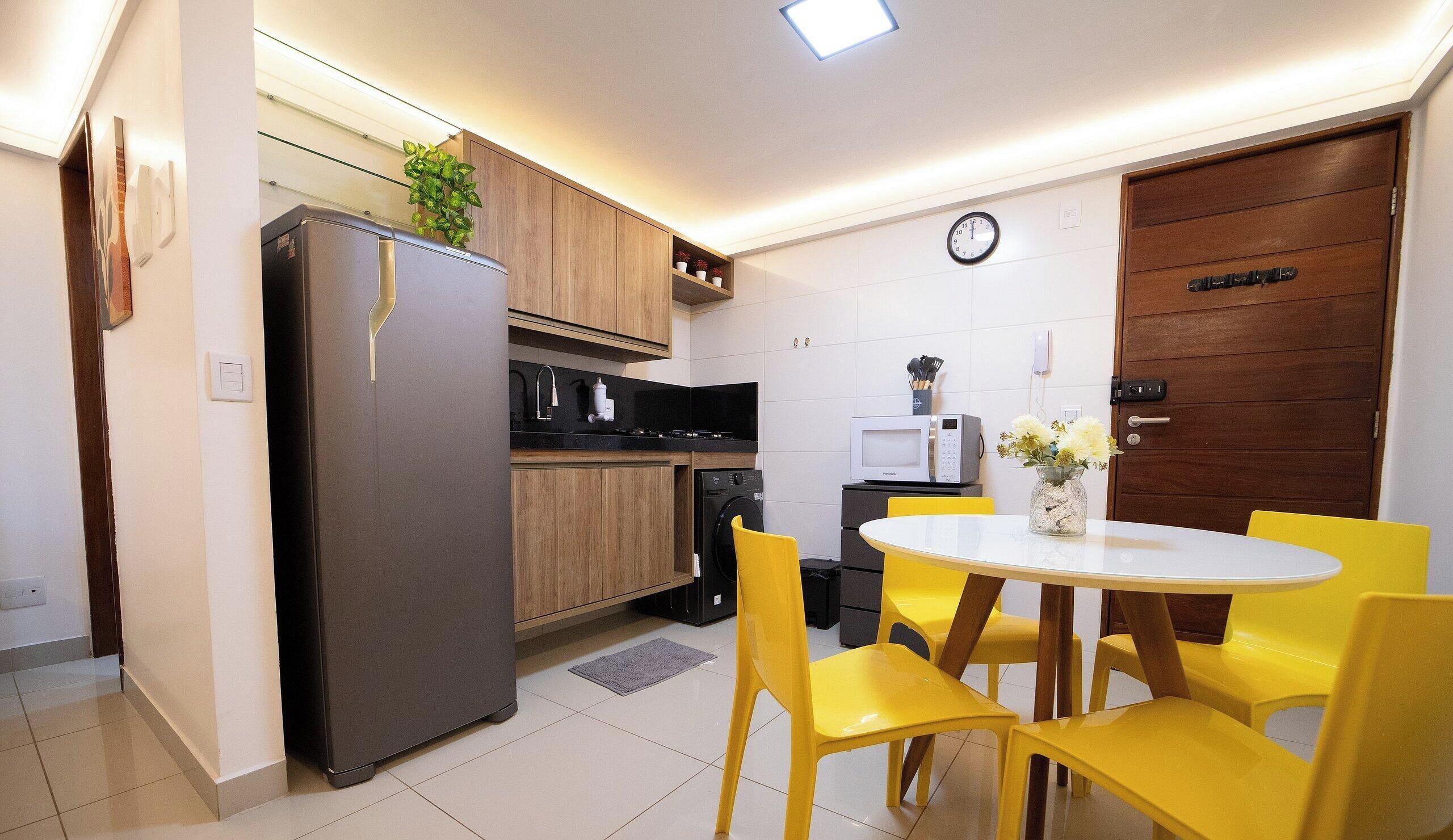 Cocina compacta con refrigerador, microondas y estufa, una mesa de comedor con sillas amarillas y una puerta de madera.