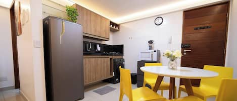A compact kitchen with a refrigerator, microwave, and stove, a dining table with yellow chairs, and a wooden door.