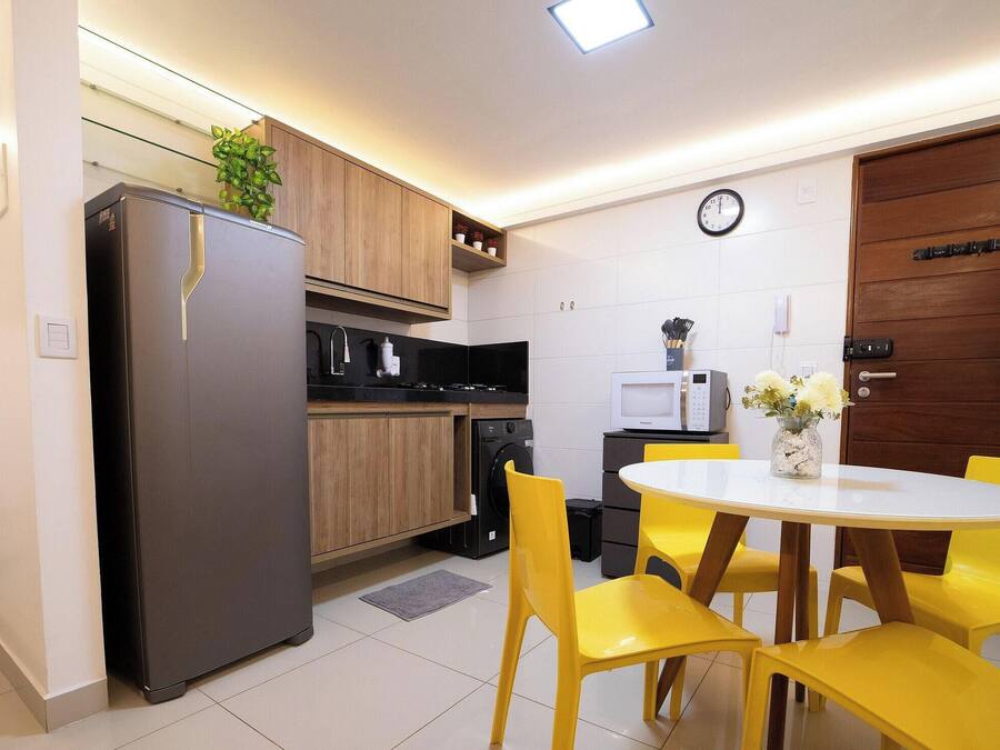 A compact kitchen with a refrigerator, microwave, and stove, a dining table with yellow chairs, and a wooden door.