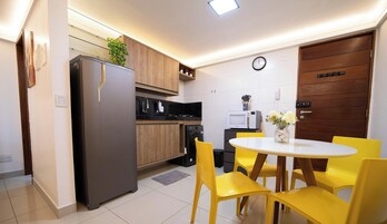 Cozinha compacta com geladeira, micro-ondas e fogão, uma mesa de jantar com cadeiras amarelas e uma porta de madeira.