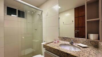 Un baño con ducha de vidrio, lavamanos de encimera de granito y un mueble de madera sobre el espejo.