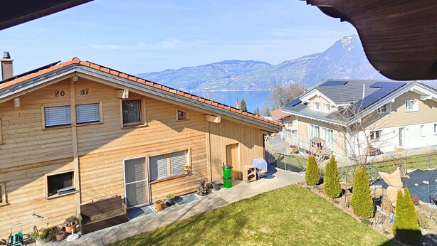 A wooden house with a sloped roof, numbered 20 and 17, with a view of a lake and mountains in the background.
