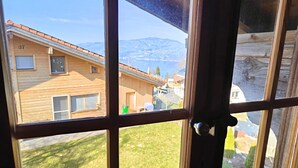 A view through a window with a wooden frame, revealing a house with a tiled roof and a number '17' on the side.