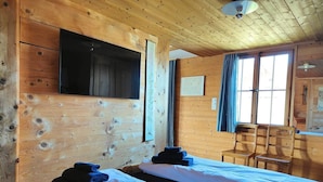 A wooden cabin room with two beds, a TV mounted on the wall, and a desk with a chair.