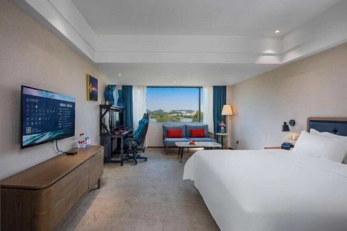Habitación de hotel con cama, escritorio con computadora, televisor, sofá y vista al exterior.