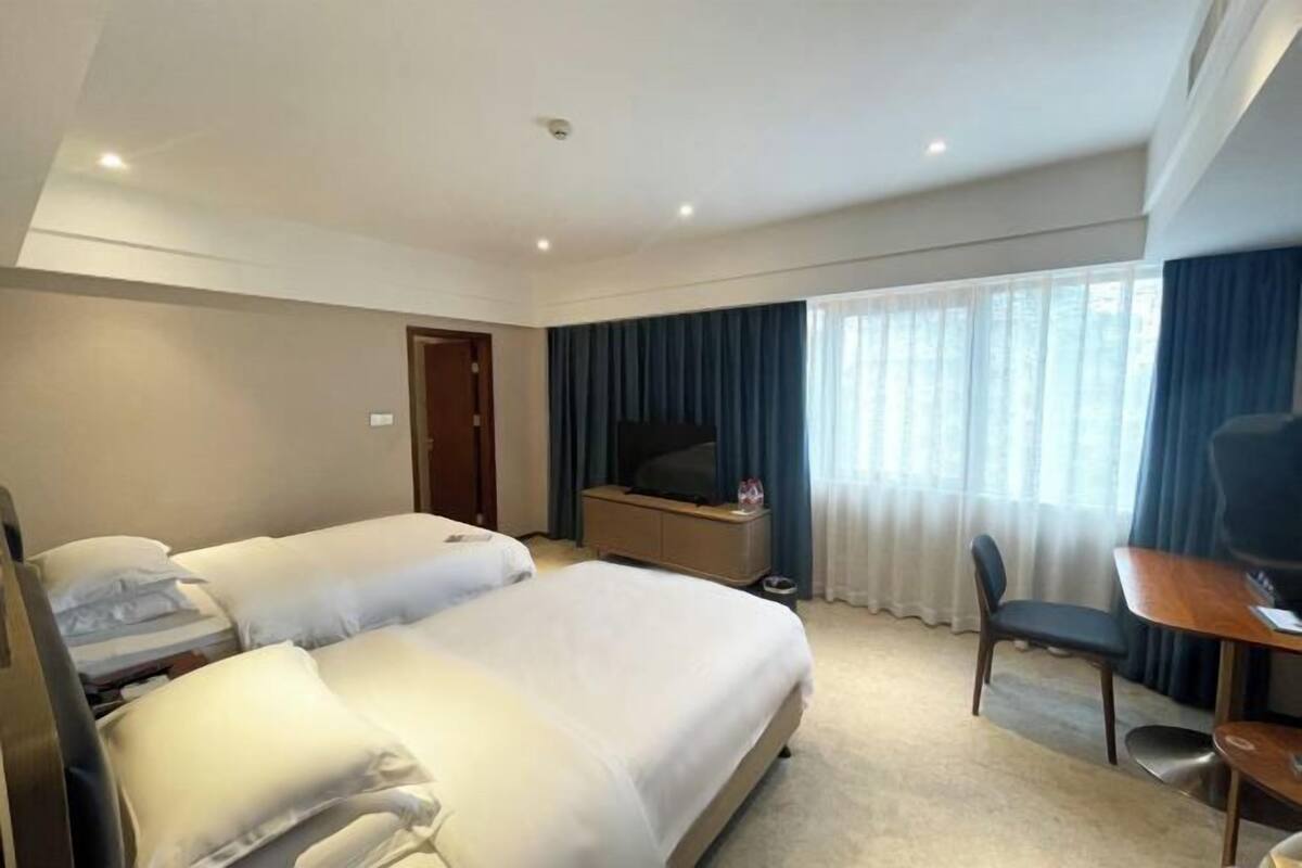 Habitación de hotel con dos camas, un escritorio, una silla, un televisor y una ventana con cortinas.