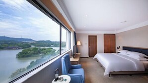 A hotel room with a large window, a bed, a chair, a small table, and a nightstand. - West Lake Garden Hotel (Huizhou)